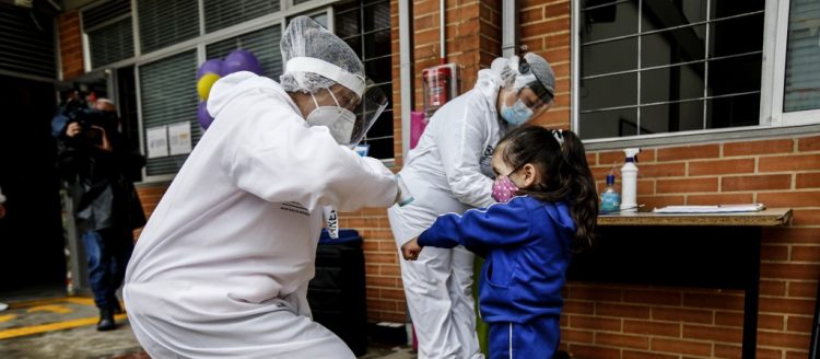 Una maestra con equipo de protección personal revisa la temperatura de una niña durante la apertura de los jardines de infancia en Bogotá, en medio de la pandemia del coronavirus COVID-19. Foto: LEONARDO MUNOZ / AFP