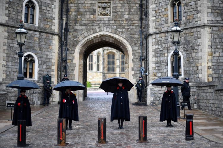 Los guardianes del castillo se refugian de la lluvia bajo los paraguas fuera del castillo de Windsor en Windsor, al oeste de Londres, el 10 de abril de 2021, el día después de la muerte del príncipe Felipe de Gran Bretaña, duque de Edimburgo, a la edad de 99 años. FOTO / AFP