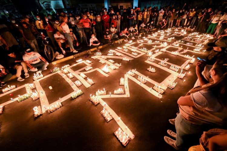 People gather around candles and words on the pavement reading "for our dead" during a vigil on May 5, 2021 in Cali, Colombia, in honor of the demonstrators who died during protests against the government of President Ivan Duque. - Thousands of people returned to the streets of Colombia on May 5 in rejection of the government of Ivan Duque, who has completed a week of pressure with demonstrations that turned violent in some cities and left some twenty people dead. (Photo by Luis ROBAYO / AFP)