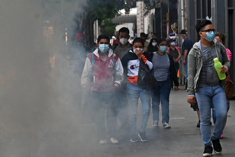 La gente pasa junto a una nube de desinfectante, mientras los trabajadores municipales rocían las calles tras un repunte en el número de casos positivos de coronavirus en Ciudad de Guatemala. Foto AFP.