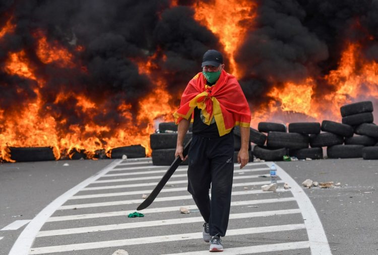 Un hombre pasa junto a neumáticos en llamas en una barricada instalada para bloquear las carreteras de acceso a la histórica ciudad de Cetinje durante una protesta contra la inauguración del nuevo jefe de la Iglesia Ortodoxa Serbia el 5 de septiembre de 2021 en Montenegro. FOTO / AFP