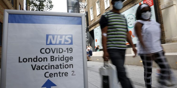 La gente pasa señales que indican la entrada al Centro de Vacunación del Puente de Londres en Londres el 9 de agosto de 2021. FOTO / AFP