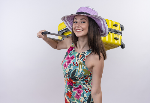 smiling young traveler woman holding suitcase on isolated white wall