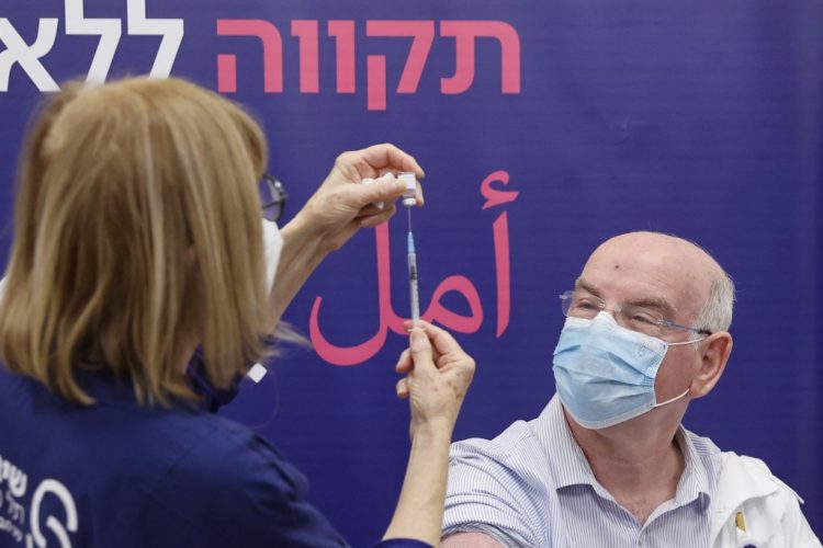 Israeli Professor Jacob Lavee receives a fourth dose of the Pfizer-BioNTech COVID-19 coronavirus vaccine at the Sheba Medical Center in Ramat Gan near Tel Aviv, on December 27, 2021, as the Israeli hospital conducted a trial of the vaccine's fourth jab on staff volunteers. Hebrew (top) and Arabic writing in the background reads: "Hope without limit." (Photo by JACK GUEZ / AFP)