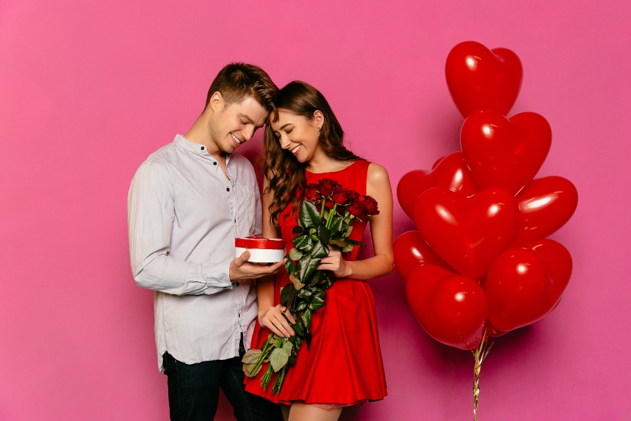 handsome man and attractive woman looking at box with gift red roses