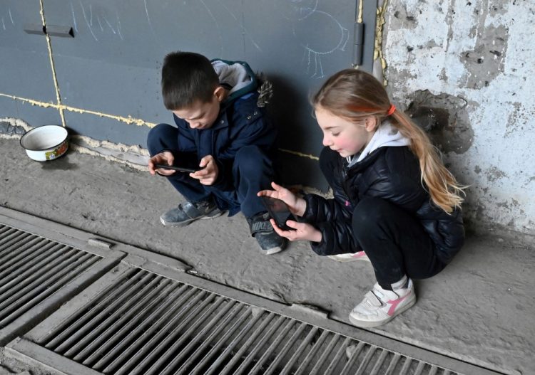 A picture taken on April 23, 2022 shows children playing with smartphones as they live in a large underground parking lot in Kharkiv, eastern Ukraine, during the Russian invasion of Ukraine. - Alina, Alex, Daniel, Kiril and Lilia are aged 8 to 14. Since the start of the war in Ukraine two months ago, they have been sleeping with their families safe from bombs in a large underground parking lot in Kharkiv, in the east of the country. The second largest city in Ukraine - nearly 1.5 million inhabitants before the war - is targeted every day by Russian rockets. Random strikes, spaced out, at any time of the day or night, sometimes deadly, and which particularly target residential areas in the north and northeast, near the front line. (Photo by SERGEY BOBOK / AFP)