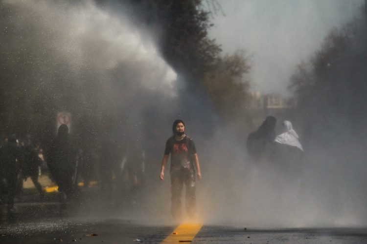 La policía antidisturbios rocía agua para dispersar a los estudiantes durante una protesta frente al palacio presidencial de La Moneda en Santiago. Foto AFP.