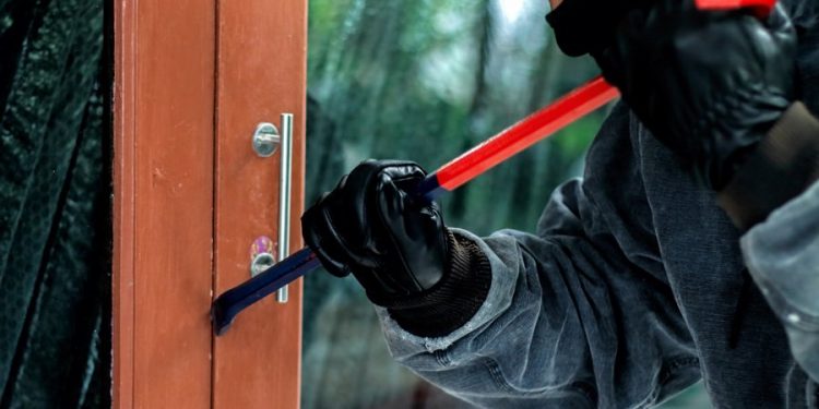 Burglar with crowbar trying break the door to enter the house
