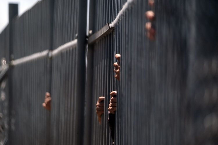 Migrantes sostienen los barrotes de la cerca del centro de detención de inmigrantes donde 39 migrantes murieron durante un incendio en Ciudad Juárez. Foto AFP.