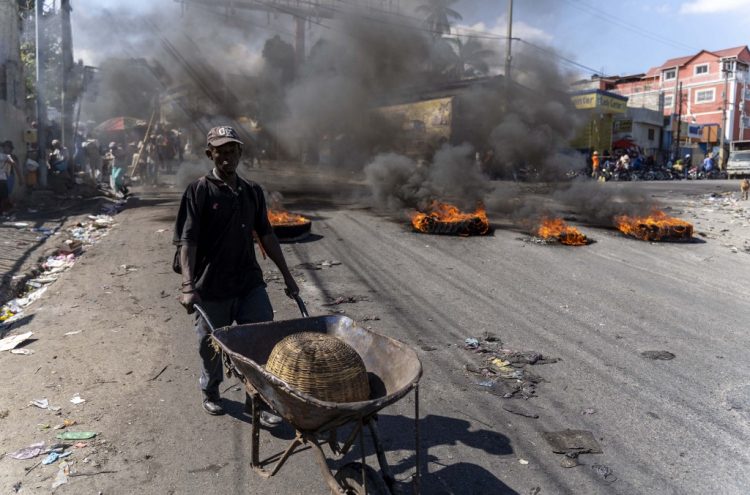 Un hombre empuja una carretilla cerca de llantas en llamas durante un día de protesta después de la muerte de seis policías en Puerto Príncipe. Foto AFP.