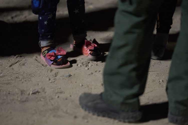 Una niña (zapatos de detalle) espera ser procesada por un agente de la Patrulla Fronteriza de Estados Unidos. Foto referencia AFP.
