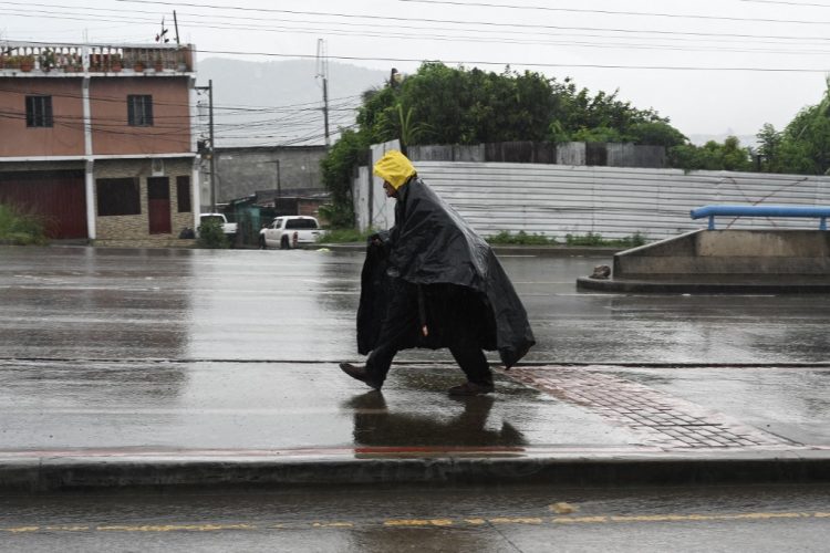 Un anciano cubierto con una bolsa de plástico camina por una calle de Tegucigalpa. Foto AFP.