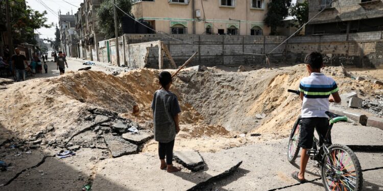 Children stand near a crater caused by Israeli bombardment in a street in Rafah in the southern Gaza Strip on May 18, 2024, amid the ongoing conflict between Israel and the Palestinian Hamas movement. (Photo by AFP)