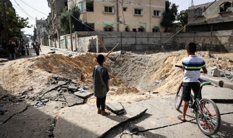 Children stand near a crater caused by Israeli bombardment in a street in Rafah in the southern Gaza Strip on May 18, 2024, amid the ongoing conflict between Israel and the Palestinian Hamas movement. (Photo by AFP)