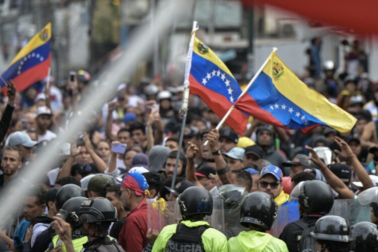 Agentes de policía hacen guardia junto a manifestantes que ondean banderas venezolanas durante una protesta contra el gobierno del presidente venezolano Nicolás Maduro en Caracas. Foto AFP.